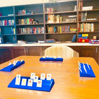 A cozy game room with a table set up for a tile-based game, surrounded by bookshelves.