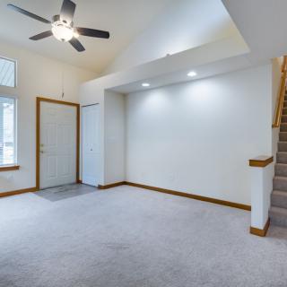 A cozy living room with carpet flooring, a ceiling fan, recessed lighting, and a staircase.