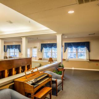 A cozy interior room featuring a piano and comfortable seating, with large windows adorned with blue curtains.