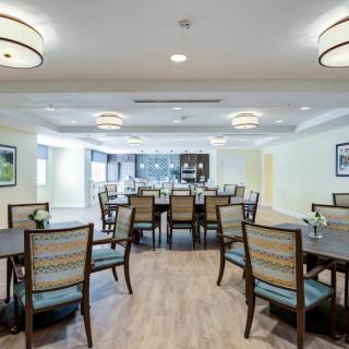 A spacious dining room with multiple tables and chairs, complemented by modern lighting and wooden flooring.