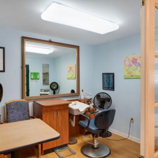 Interior of a small hair salon with a mirror, chair, and desk.