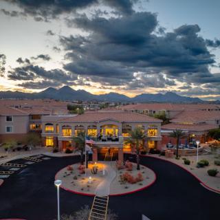 A picturesque view of a hotel at sunset, surrounded by mountains and dramatic clouds.