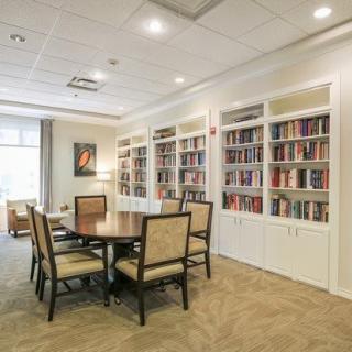 A cozy library reading room with bookshelves, a round table, and chairs.