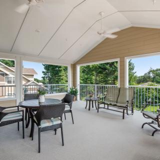 A spacious covered patio with outdoor furniture and ceiling fans, offering a view of greenery.