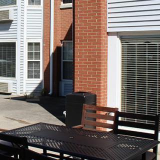 A sunny outdoor patio area with a table and chairs near a brick apartment building.