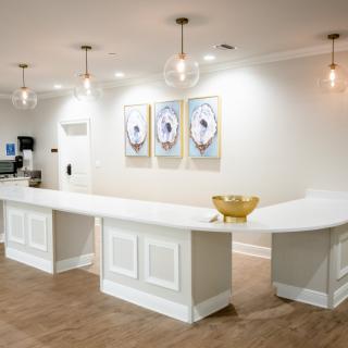 A modern reception area featuring a white counter, pendant lighting, and artwork on the wall.
