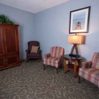 A cozy living room area featuring two striped armchairs, a side table with a lamp, and a wooden cabinet.