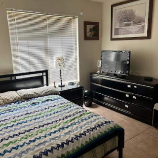 A cozy bedroom featuring a striped bedspread, modern furniture, and a large window.
