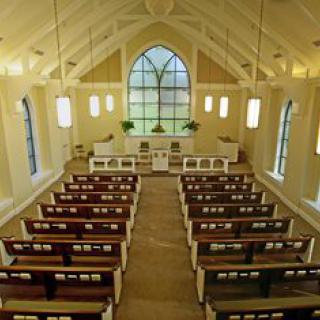 Interior of a church with wooden pews and large windows.