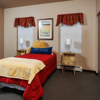 A cozy bedroom with a single bed, nightstands, and decorative lamps next to two windows.