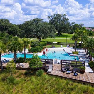 A serene outdoor pool area surrounded by lush greenery and a wooden deck, under a partly cloudy sky.