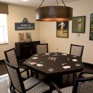 A cozy game room featuring a poker table surrounded by chairs, with sports-themed wall decor and ambient lighting.