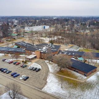 An aerial view of a school campus surrounded by winter scenery and a parking lot.