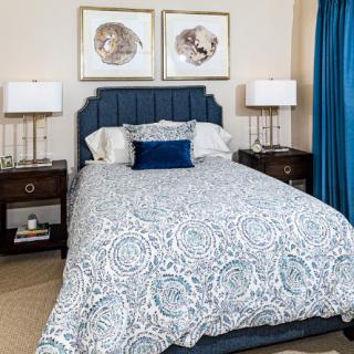 A stylish bedroom with a patterned comforter, framed artwork, and modern bedside lamps.