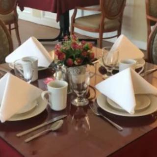 A neatly arranged dining table with plates, cups, cutlery, and a flower centerpiece.