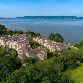 Aerial view of a residential complex by the river, surrounded by lush greenery.