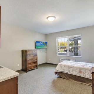 A minimalist bedroom featuring a bed, dresser, and wall-mounted TV with natural light coming through the window.