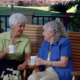 Two elderly women enjoying a cheerful conversation over coffee in a serene outdoor setting.