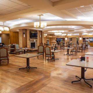 A spacious dining area with neatly arranged tables and chairs, featuring wooden flooring and modern lighting.