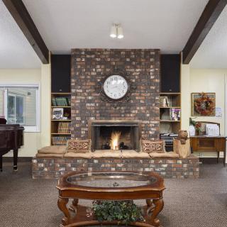 A cozy living room featuring a brick fireplace with a clock above, wooden beams, and a coffee table in the center.