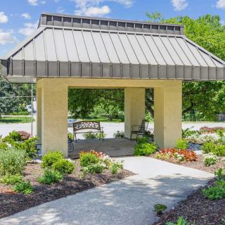 A charming gazebo surrounded by a lush garden with blooming flowers and a paved pathway.