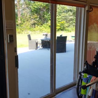 A view through a sliding door opening to a patio with outdoor furniture, surrounded by greenery.