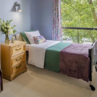 A cozy bedroom with a neatly made bed and a large window revealing lush greenery outside.