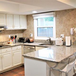 A modern kitchen with white cabinets and granite countertops, featuring various appliances and a large window.