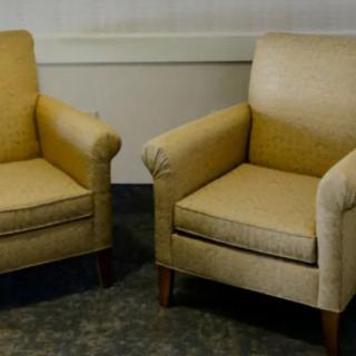 A pair of beige upholstered armchairs placed side by side on a carpeted floor.
