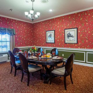 A traditional dining room with a round table, set for a meal, surrounded by elegant chairs and decorated with red wallpaper and framed artwork.