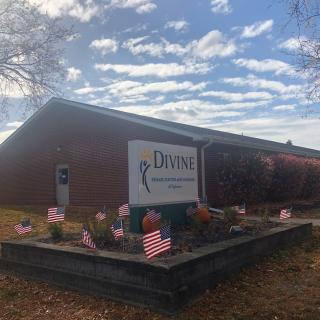 A building with a prominent sign in front, surrounded by small American flags and landscaping under a partly cloudy sky.