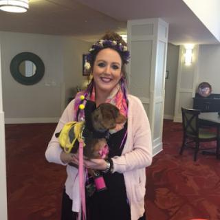 A cheerful woman poses with her dog in a cozy lobby setting.