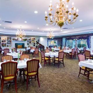 An elegant dining room with chandeliers, set with multiple tables and chairs.