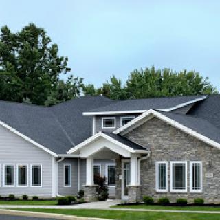 A beautifully designed modern house featuring a mix of stone and siding, surrounded by greenery.