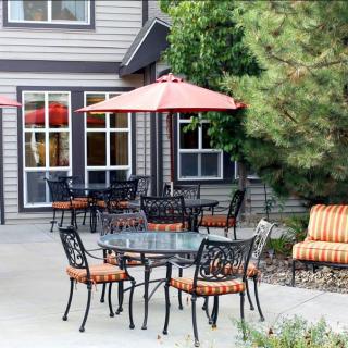 A cozy outdoor patio area featuring metal chairs with striped cushions, a glass-top table, and red umbrellas.
