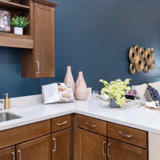 A modern kitchen with wooden cabinets, a white countertop, and decorative vases against a blue wall.