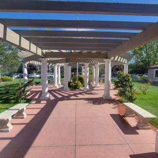 A scenic outdoor pergola with benches surrounded by a garden setting.