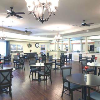 A spacious dining room with multiple tables and chairs, featuring elegant chandeliers and ceiling fans.