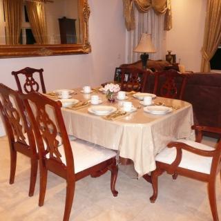 A neatly set dining table in an elegant dining room with a large mirror and draped curtains.
