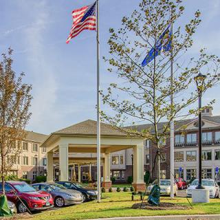 A building entrance with parked cars, surrounded by trees and flags waving.