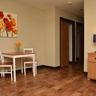 A cozy dining area with a wooden floor, featuring a small table and chairs near an artwork and hallway.