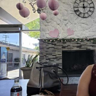A cozy cafe interior with a wall clock, pink decorations, and a table with a handbag and drink.