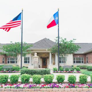 A building with American and Texas flags surrounded by landscaped gardens and flowers.