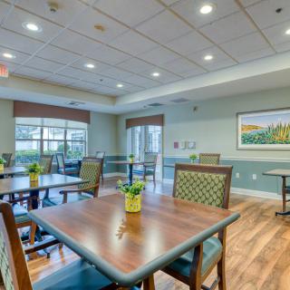A well-lit dining area with wooden floors and neatly arranged tables and chairs.