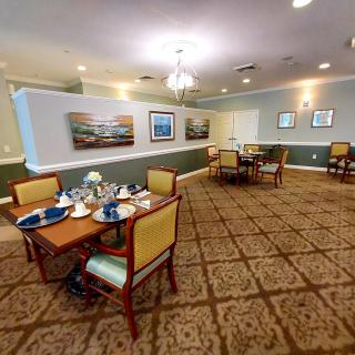 A well-lit dining room with neatly arranged tables and chairs, decorated with paintings on the walls.