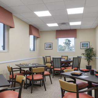 A well-lit dining room with multiple tables and chairs, featuring large windows and wall decorations.
