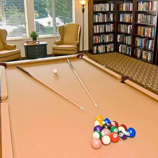 A cozy game room with a pool table and a library area featuring bookshelves and comfortable chairs.