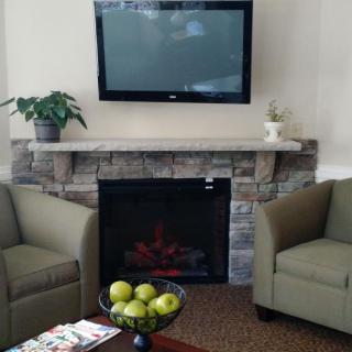 A modern living room with a wall-mounted TV above a fireplace, flanked by two green chairs and a bowl of green apples on the table.