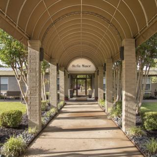 Covered walkway leading to a building entrance surrounded by greenery.
