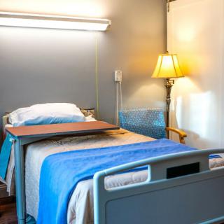 A hospital room featuring a single bed with blue linens, a bedside table, and a lampshade.